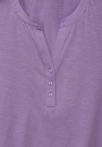 Maglietta henley lavanda con scollo a V, cinque bottoni lungo il soffietto e un tessuto morbido e testurizzato con un sottile motivo mélange.