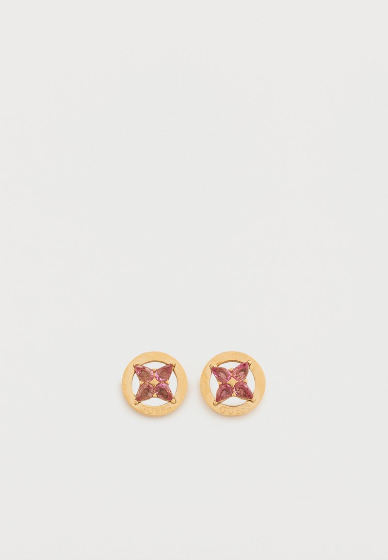 Σκουλαρίκια καρφωτά με χρυσή απόχρωση που διαθέτουν κυκλικό σχέδιο με λεπτομέρεια ρόζ πολύτιμου λίθου σε σχήμα που μοιάζει με λουλούδι. Το "GUESS" είναι χαραγμένο στην άκρη.