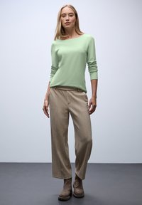 Lichtgroene lange mouwtop gecombineerd met beige, wijde broekspijpen. De outfit heeft een zachte textuur, met een eenvoudig ontwerp en geen zichtbare patronen.