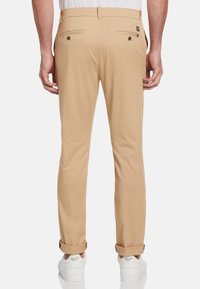 Kaki chinos met een gladde textuur, twee achterzakken met knopen en opgerolde mouwen, gecombineerd met witte sneakers.
