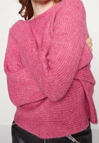 Pull rose tricoté à coupe ample, manches côtelées et motif texturé. L'ourlet inférieur est légèrement plus long à l'arrière.