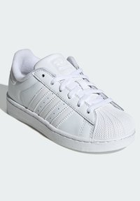 Bijela kožna tenisica s teksturiranim vrškom, vezicama sprijeda i trima bočnim prugama. Izdvojeni brend na jeziku i bočnoj strani.