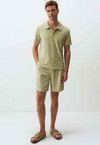 Jasnozielona koszulka polo z kołnierzykiem, w komplecie z dopasowanymi szortami. Model nosi brązowe klapki. Miękka tekstura, casualowy styl.