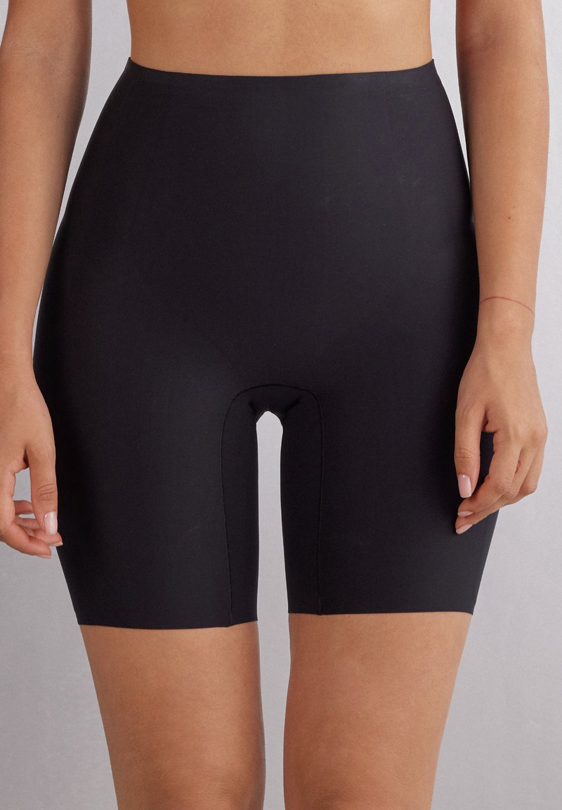 Černé vysoké tvarující šortky vyrobené z elastického materiálu, s hladkou texturou a délkou do poloviny stehna, s výřezem ve středu.
