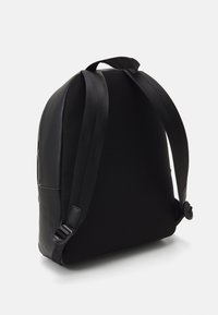 Zaino nero con schienale in rete testurizzata, dettagli in pelle liscia, spallacci regolabili e una forma snella per facilitare l'uso.