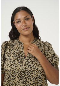 Blus med leopardmönster i beige med svarta fläckar. Har V-ringning och puffärmar, tillverkad av ett mjukt och lätt tyg.