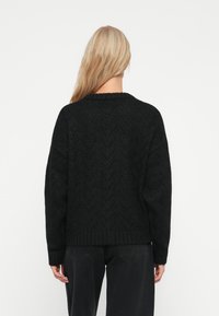 Svart gestrikket genser med zigzag-mønster, rund hals og ribbestrikket nederkant. Oversized passform med senkede skuldre og strukturert stoff.