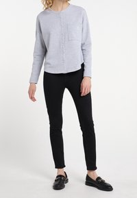 Camicetta grigia chiara con scollo rotondo, dotata di taschino sul petto e ricamo di ancore discreto, abbinata a pantaloni neri slim-fit.