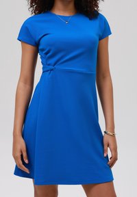 Modré šaty z texturované látky s kulatým výstřihem, krátkými rukávy a bočním uzlem, se zvonovou sukní.