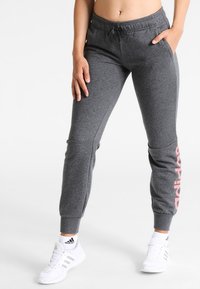 Grijze joggerbroek met een elastische tailleband, trekkoord en roze "adidas" logo op de zijkant. Het materiaal lijkt zacht en textuur te hebben.