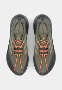 Paar olivgrüne und schwarze Sportschuhe mit orangefarbenen Bungee-Schnürsenkeln, die in einem sicheren, überkreuzten Muster gebunden sind, von oben auf weißem Hintergrund.
