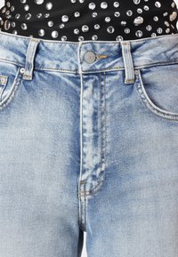Light blue denim jeans with faded patches. Features a classic button closure, five pockets, and contrasting yellow stitching.