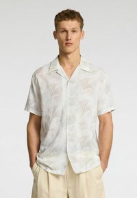 Kortærmet skjorte med krave i let, tekstureret stof med et blomsterprint i lyse farver. Har knapper ned langs fronten.