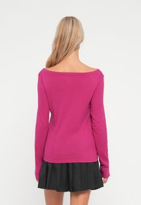 Fuksija dugouhih rukava s off-shoulder izrezom. Mekani materijal, uski kroj, u kombinaciji s crnom suknjom s nabranim detaljima do pola bedra.