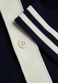 Navy knitted polo shirt featuring white striped collar, button closure, and ribbed texture. Smooth fabric with classic design elements.
