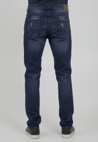 Dark blue denim jeans with a straight fit, featuring distressed details, two back pockets, and a leather patch at the waistband.
