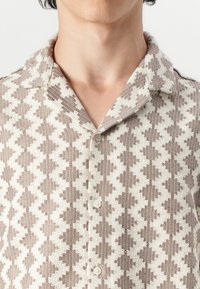 Short-sleeve button-up shirt in beige and cream with a zigzag pattern, textured fabric, and a classic collar design.