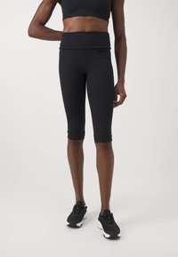 Leggings capri atletici neri con vita alta, caratterizzati da una texture liscia e una vestibilità aderente, abbinati a sneaker nere.