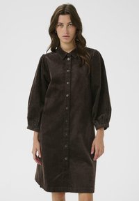 Brown corduroy dress with a collared neck, button closure, balloon sleeves, and a straight cut. Features textured vertical ribbing.