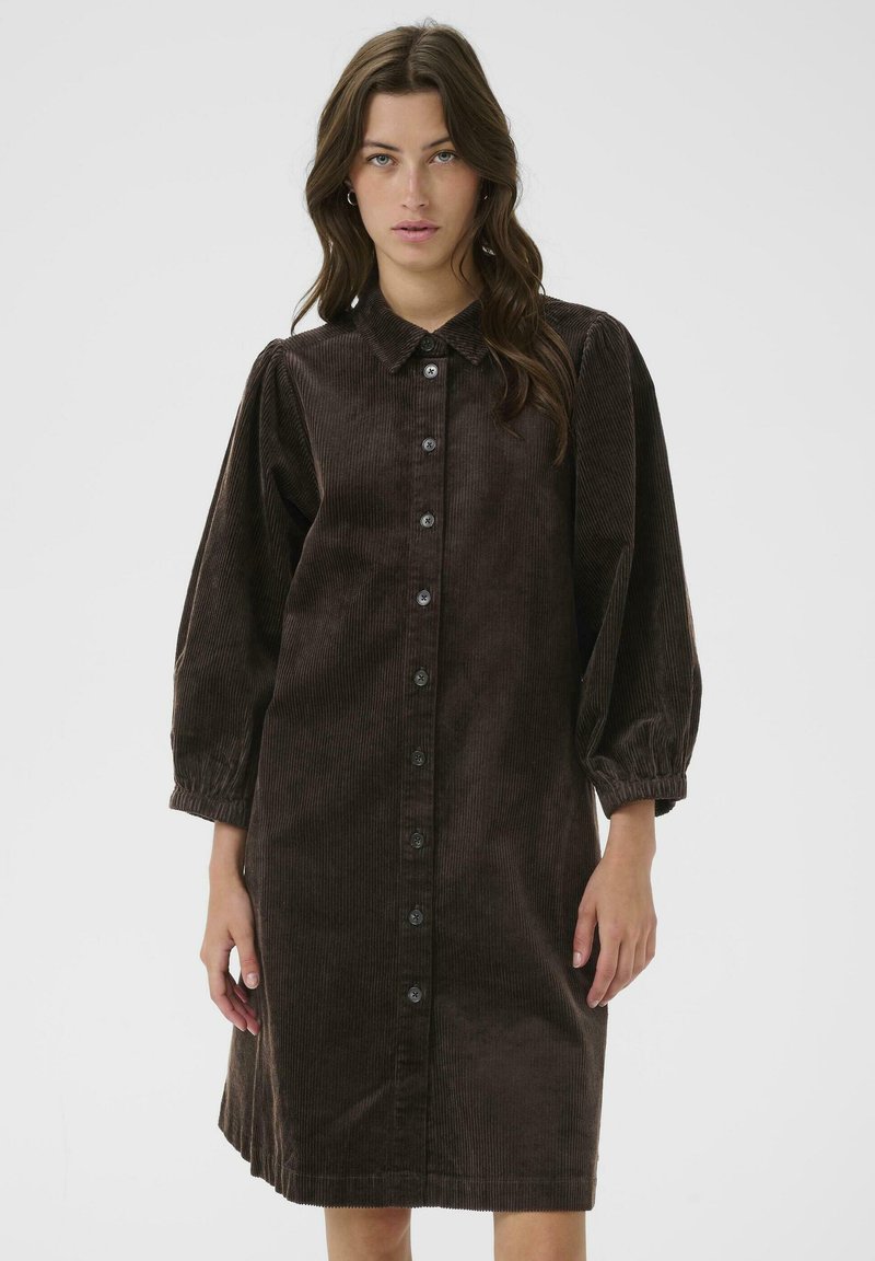 Brown corduroy dress with a collared neck, button closure, balloon sleeves, and a straight cut. Features textured vertical ribbing.