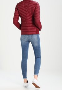 Punainen puffatakki, jossa on vaakasuorat tikatut osat, korkea kaulus ja lyhyt malli, yhdistettynä vaaleansinisiin skinny-farkkuihin ja valkoisiin lenkkareihin.