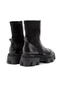 Zwarte enkellaarsjes met een gladde leren afwerking, chunky geprofileerde zool en een gestructureerd zwart platform. Trekbandjes achteraan voor gemakkelijk aan- en uittrekken.