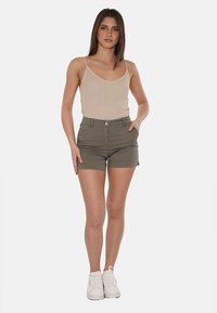 Top in raso beige a costine abbinato a pantaloni corti verde oliva con chiusura frontale a bottoni e orlo arrotolato. Il modello indossa sneakers bianche.