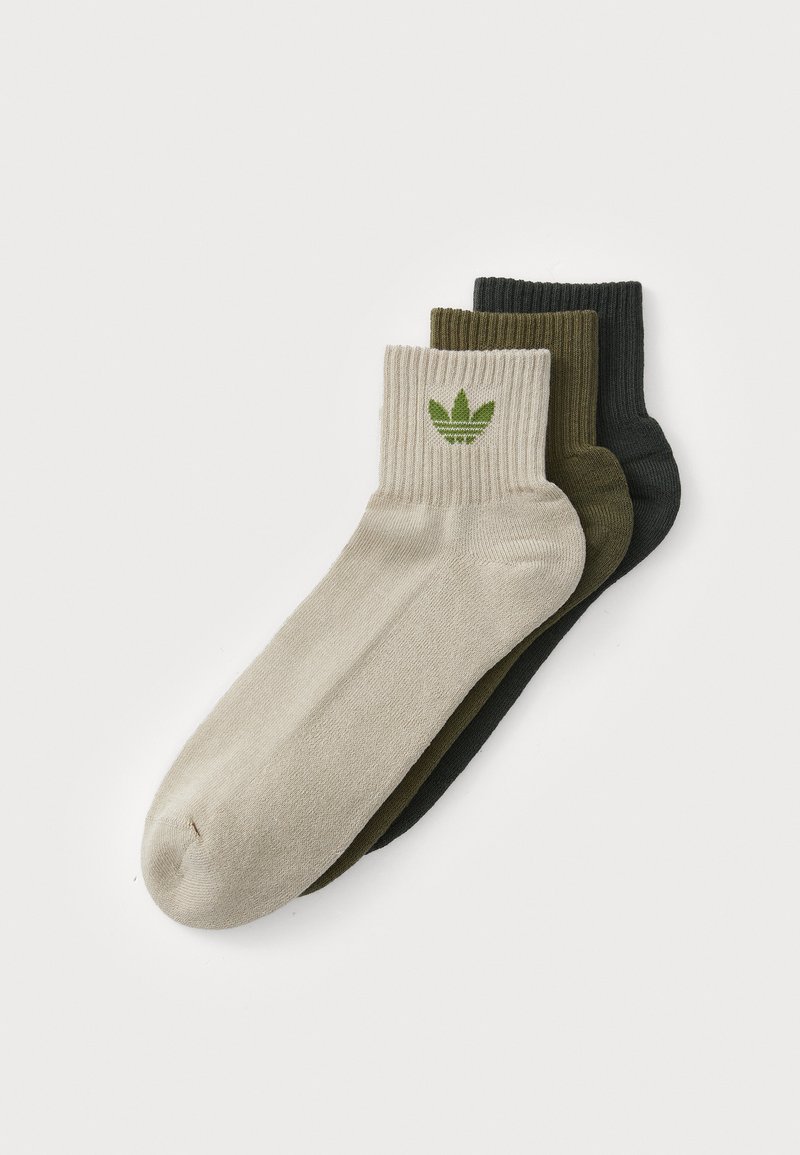 Tri par sock z ribastim robom. Barve: bež, olivno zelena in črna. Vsak par prikazuje zeleni logo na robu.