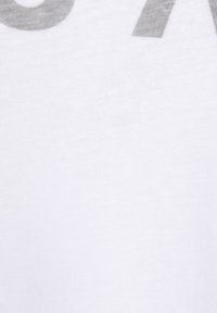 Weißer Baumwollstoff mit glatter Textur, der schwache graue Buchstaben zeigt. Der Fokus liegt auf dem schlichten Design und der Farbe des Textils.