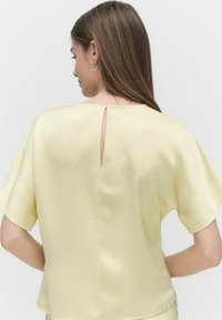 Gul satin top med korte flæser på ærmerne og en nøglehulslukning i ryggen. Blød tekstur, afslappet pasform og minimalistisk design.