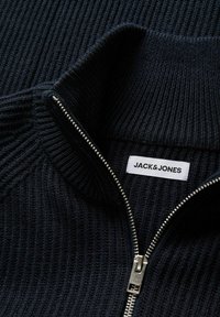 Pull en maille côtelée noir avec une fermeture éclair argentée partiellement ouverte et une étiquette blanche Jack & Jones visible au col.