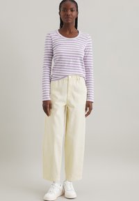 Lila und weiß gestreiftes Langarmshirt kombiniert mit hellgelben weiten Hosen und weißen Turnschuhen, mit Rundhalsausschnitt und lässiger Passform.