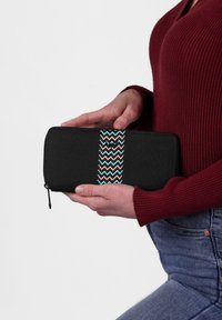 Black wallet with a zip closure, featuring a central woven pattern of zigzag in pink, blue, and white. Made of durable fabric.