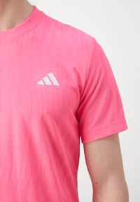 Pink athletic t-shirt featuring a textured design, round neck, and short sleeves. Includes a contrasting white logo on the left side.