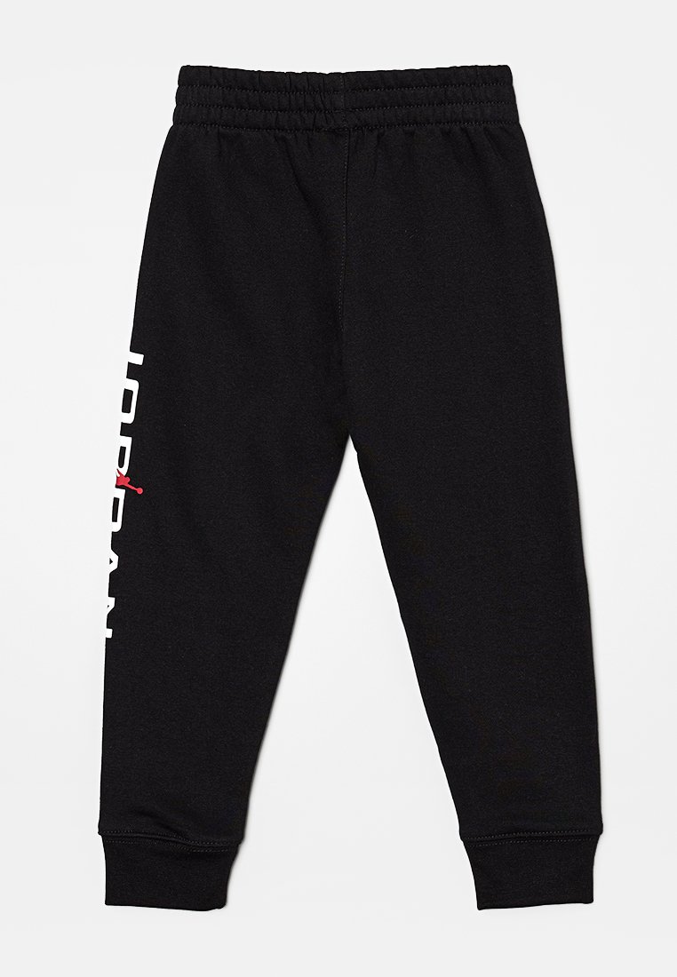 Black jogger pants with an elastic waistband, featuring "JORDAN" in white text along the side and a small red logo. Soft fabric.
