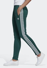 Zielone spodnie sportowe z białymi paskami po bokach, wykonane z gładkiego materiału. Posiadają wygodne dopasowanie i kieszenie na zamek.