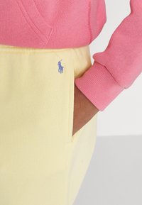 Rosa sweatshirt av tyg med ribbat ärm, matchad med gula sweatpants som har en liten blå broderad logotyp. Mjuk textur, avslappnad passform.