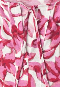 Gros plan d’un tissu à motifs floraux roses et rouges avec des plis cousus sur un fond blanc texturé.