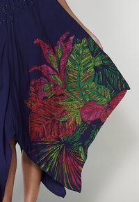 Robe marine ornée de broderies florales vibrantes en rouge, rose, vert et jaune. Ourlet fluide avec une coupe asymétrique et une texture textile douce.