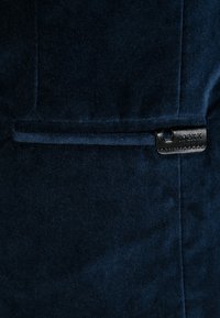 Marineblauwe stof met een zachte textuur, voorzien van een horizontale zak en een zwart leren accent met stiksel details.