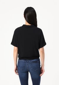 Black short-sleeve shirt with a collar, smooth fabric, relaxed fit, paired with dark blue fitted jeans featuring back pockets.
