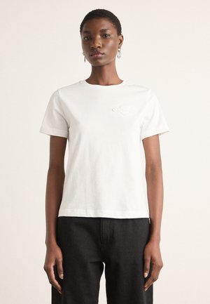 T-shirt en coton blanc avec un col rond et des manches courtes. Doté d'un logo brodé subtil sur la poitrine gauche. Forme simple et classique.