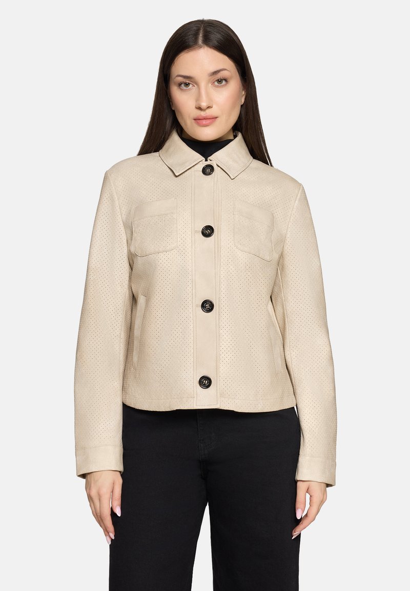 Beige leren jas met perforaties, een kraag, zakken aan de voorkant en zwarte knopen. Gestyled met een zwarte top en donkere broek.