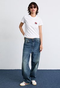 Vit bomullst-shirt med körsbärsgrafik, kombinerad med lösa blå jeans och vita sneakers med röda och marinblå detaljer.