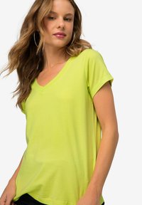 T-shirt verde lime a V, realizzata in materiale morbido, maniche corte, vestibilità rilassata. Sullo sfondo è presente un bianco senza motivi visibili o disegni.