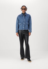 Jeansjakke med quiltet design, to frontlommer, krage og knapper; kombinert med svarte bukser i imitert skinn som flarer og svarte sportssko.