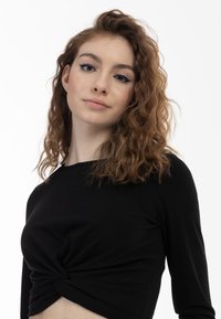 Top a maniche lunghe nero a costine con un design frontale torcido, caratterizzato da una silhouette aderente e una consistenza morbida su uno sfondo bianco.