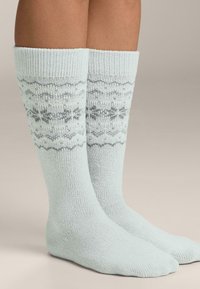 Svetlo modre nogavice do kolen z rebrasto teksturo in sivo snežinko vzorec. Mehki material z oprijetim prileganjem okoli meč in gležnjev.