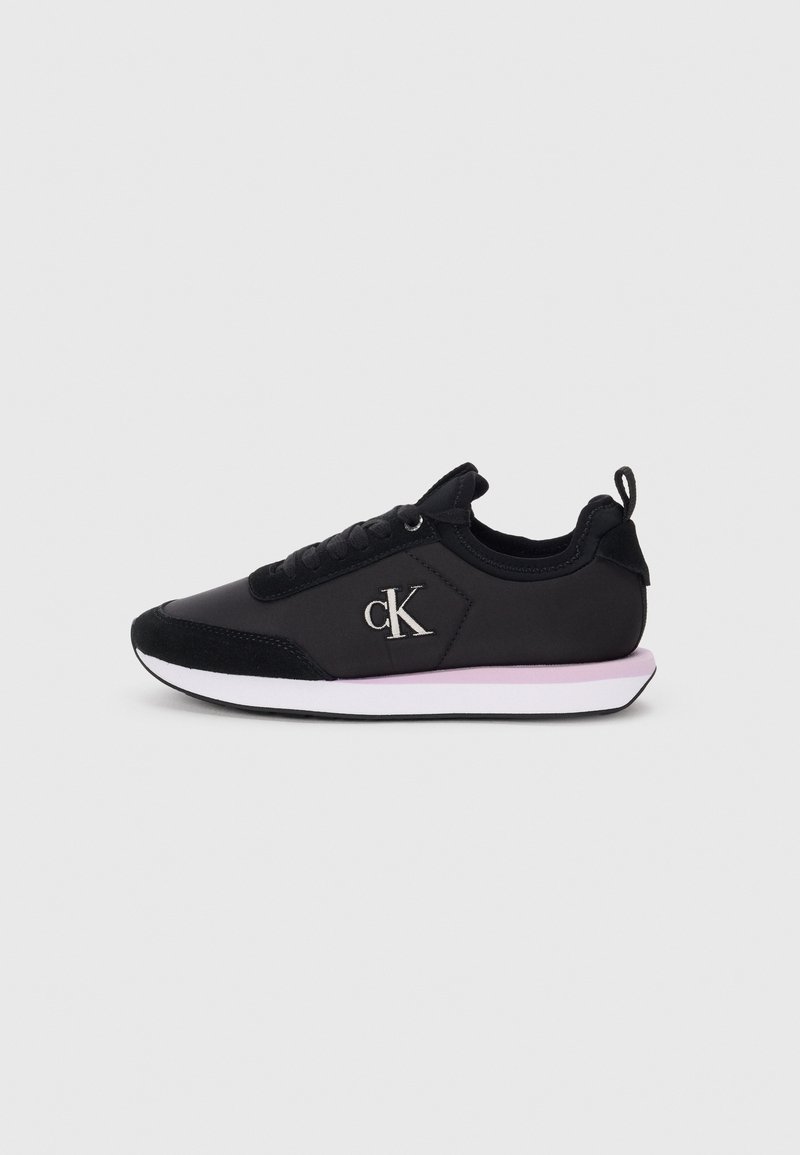 Black athletic sneaker with fabric and suede panels, featuring laces, a silver logo, and a white-pink sole. Side view.