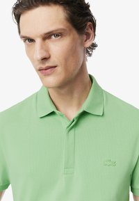 Grön polo skjorta i texturerad bomull, med krage, knappslå och broderad logotyp på vänster bröst.